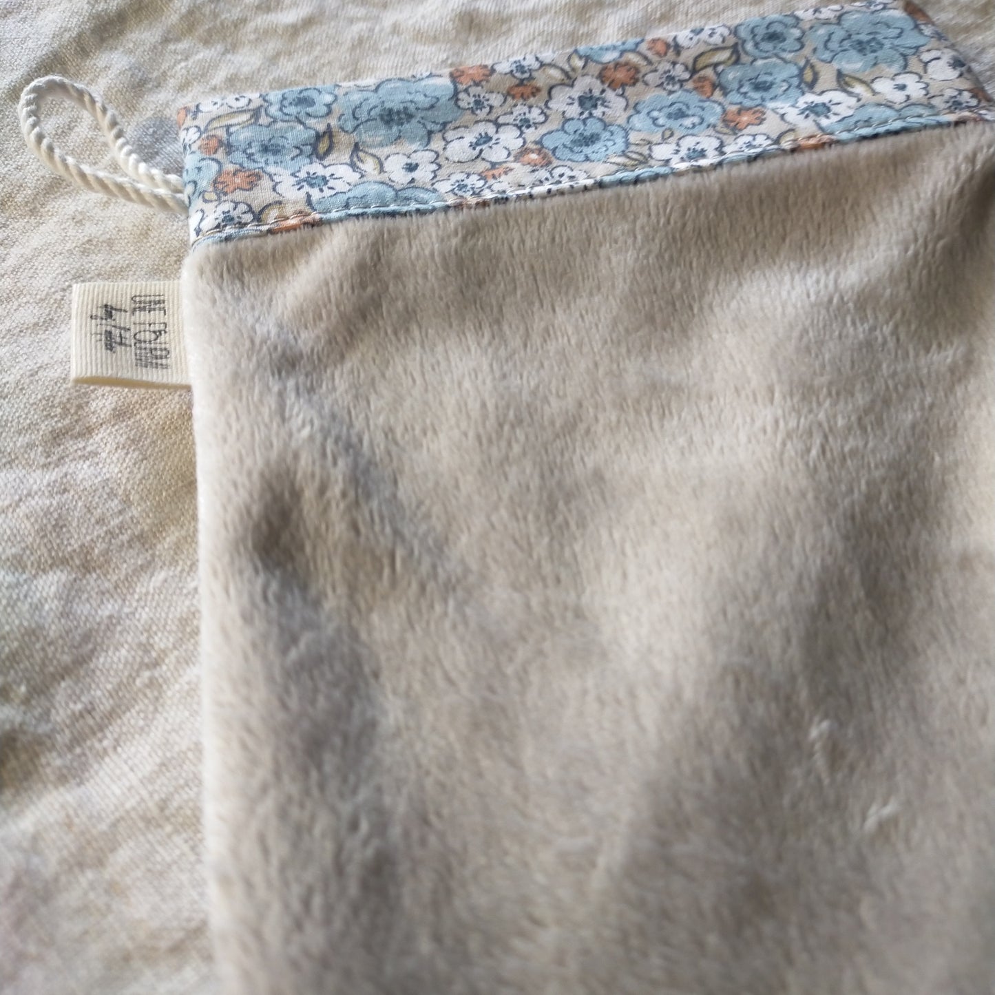 zoom sur le haut du gant bleu et taupe avec le cordon de suspension et l'étiquette de la marque Une fourmi dans l'atelier
insérée dans la couture.