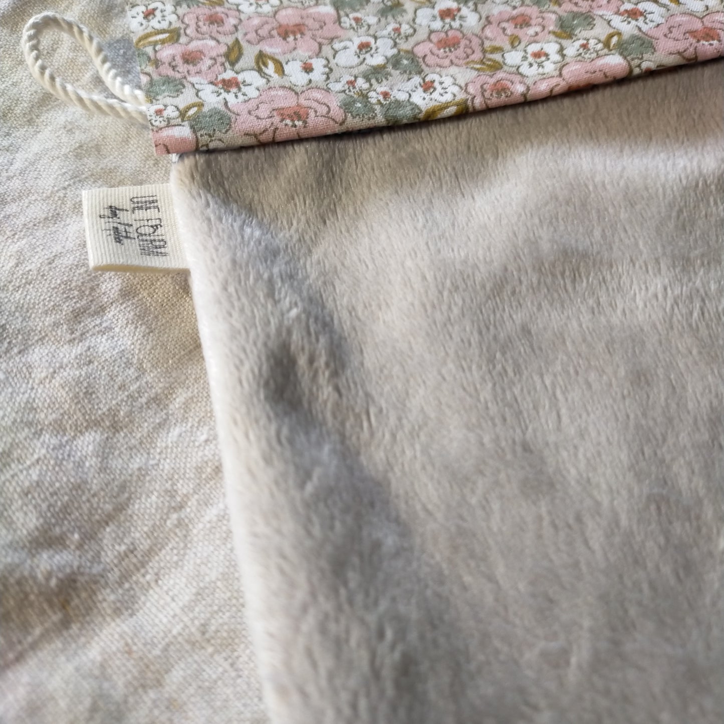 zoom sur le haut du gant rose et taupe avec le cordon de suspension et l'étiquette de la marque Une fourmi dans l'atelier
insérée dans la couture.