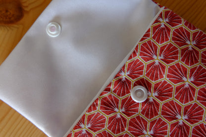 zoom sur une pochette à savon rouge aux motifs d'écailles ouverte avec vue sur la doublure imperméable blanche et la fermeture à pression.