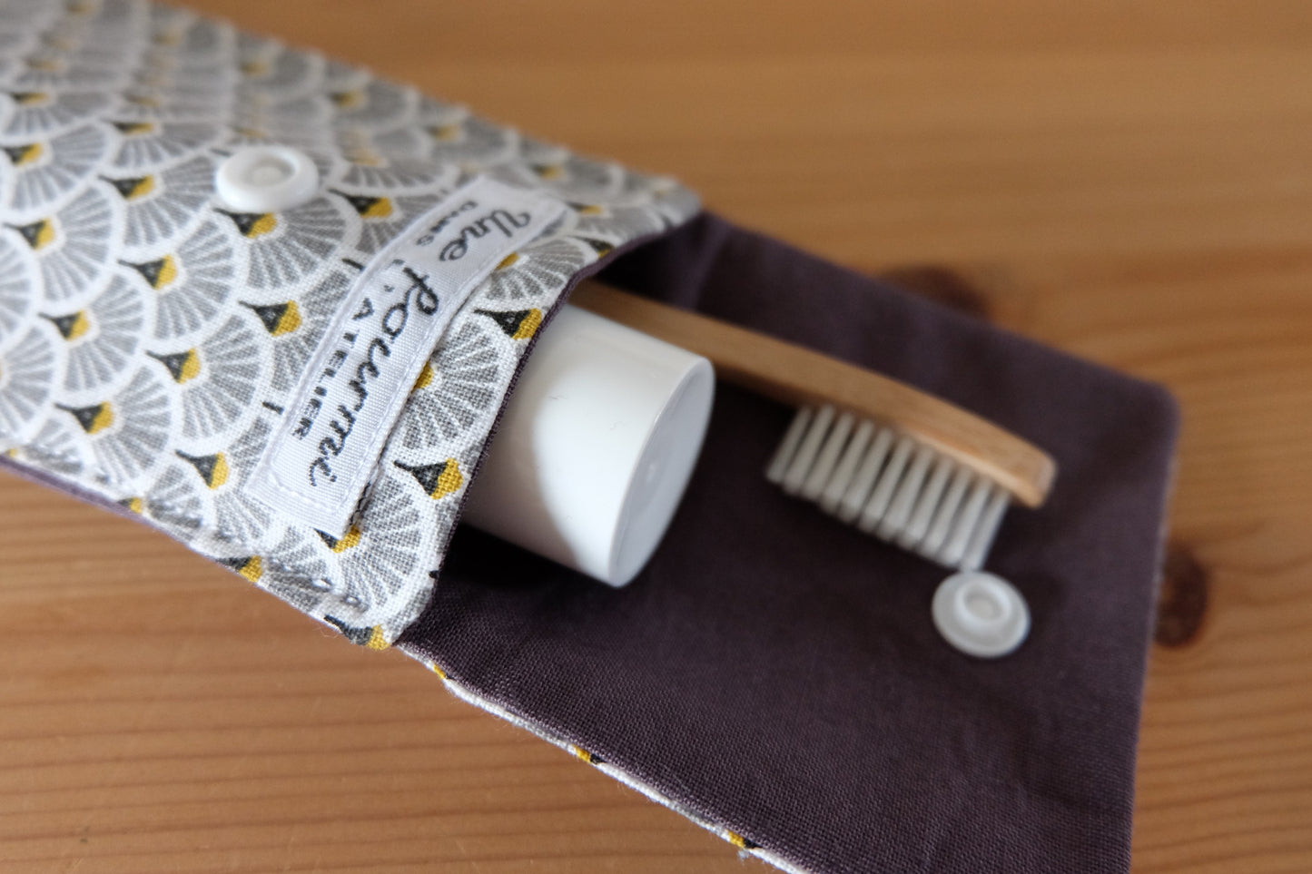 zoom sur le rabat ouvert d'un étui pour brosse à dent gris. doublure grise, avec à l'intérieur un tube de dentifrice et une brosse à dent. fermeture avec une pression blanche.