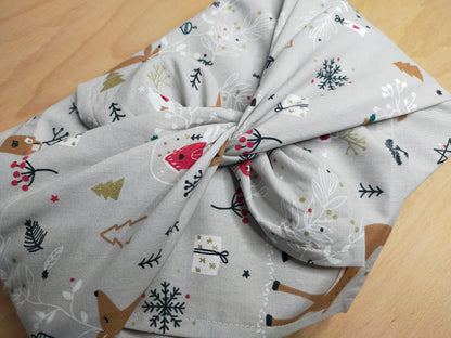 furoshiki sur le thème de Noel avec un tissus dans les tons gris, beige, blanc, rouge avec motifs de biches et cadeaux. emballage cadeau réutilisable et lavable, accessoire écologique et zéro déchet.