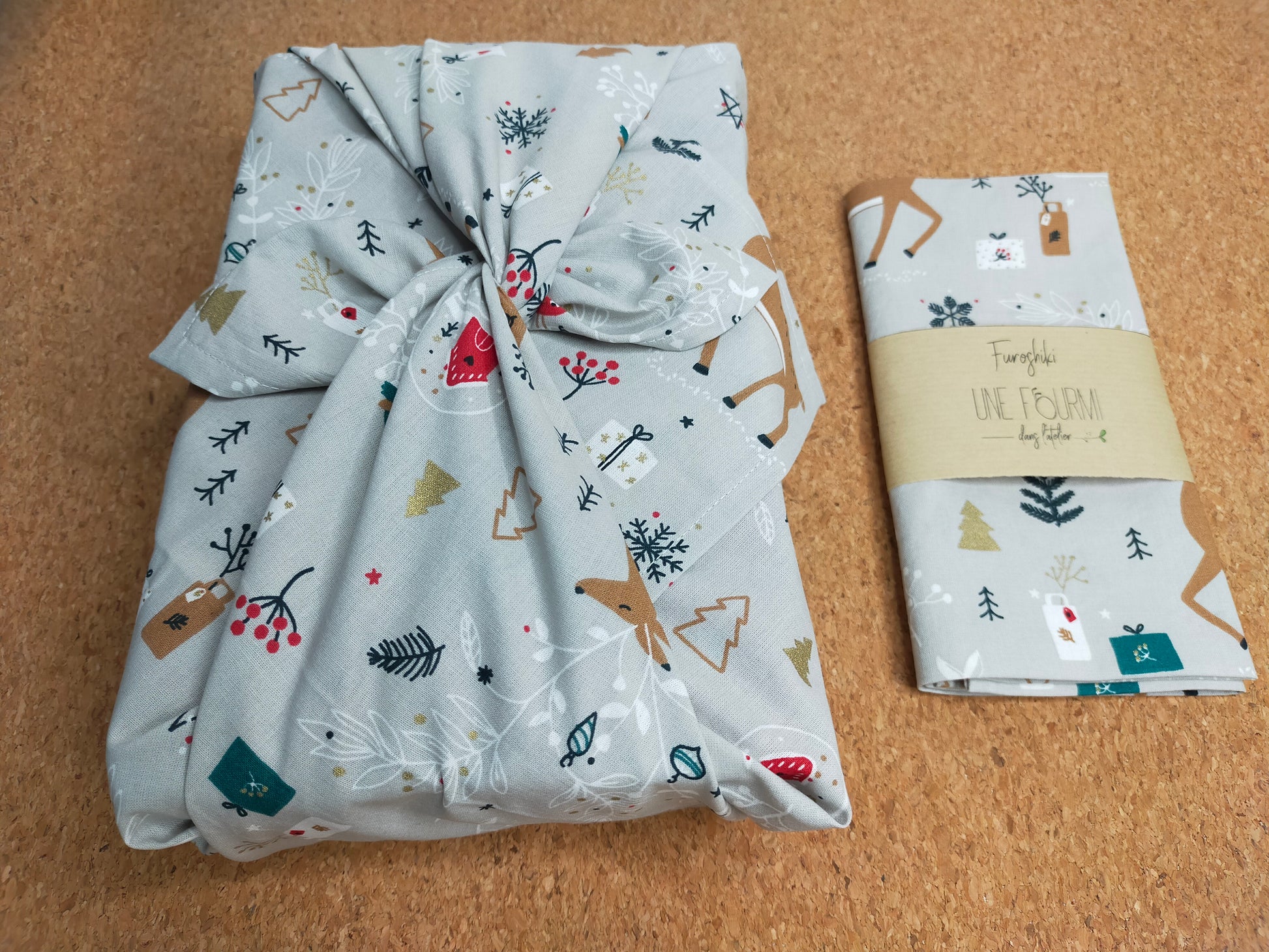 furoshiki sur le thème de Noel avec un tissus dans les tons gris, beige, blanc, rouge avec motifs de biches et cadeaux. emballage cadeau réutilisable et lavable, accessoire écologique et zéro déchet.