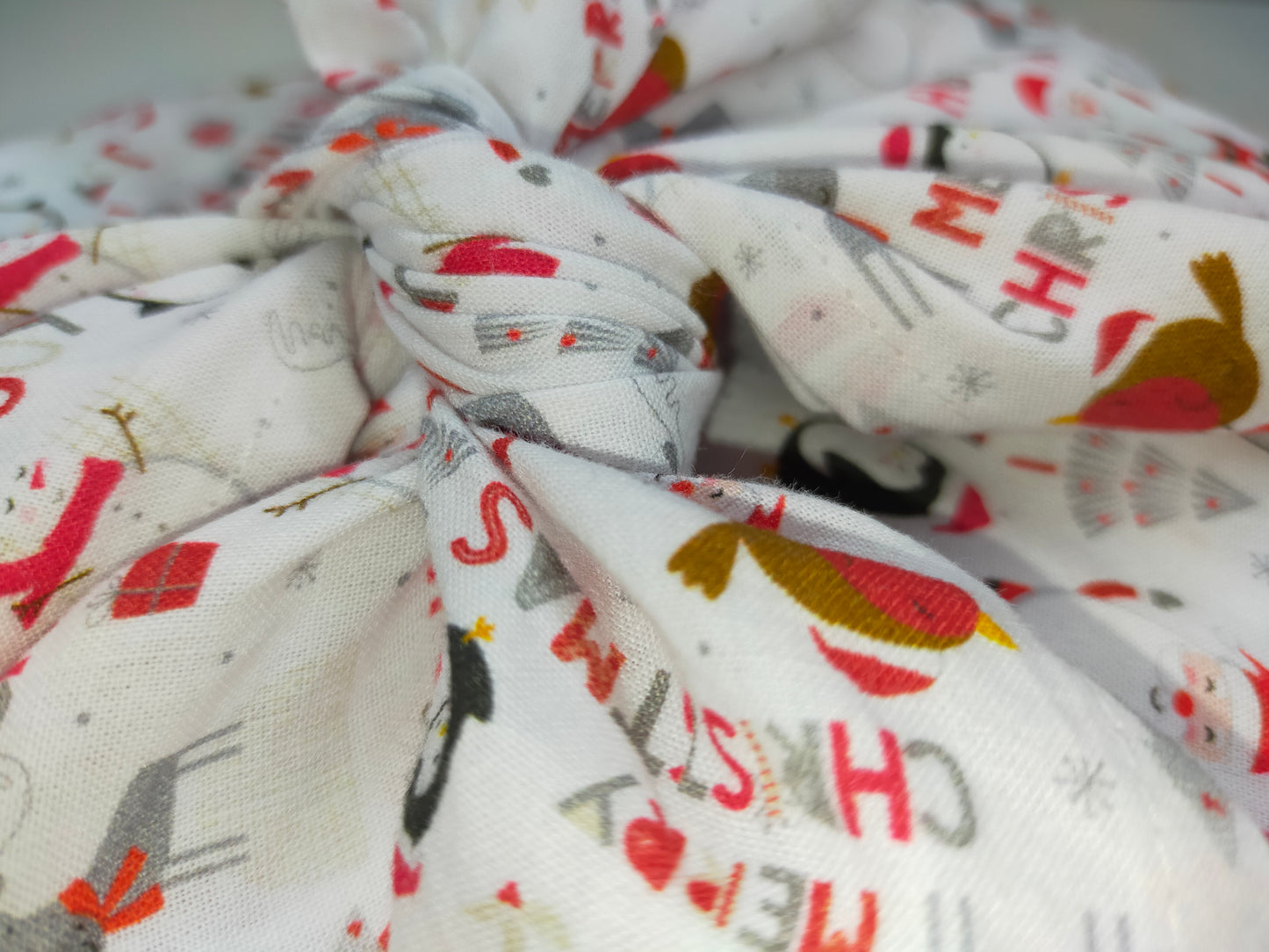 zoom sur le nœud du furoshiki en coton de couleur blanche avec des motifs de père noel et pingouins et des inscriptions merry christmas. emballage cadeau réutilisable et lavable