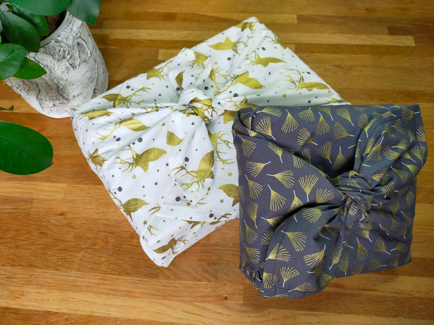 Furoshiki avec 2 tissus différents, l'un gris aux motifs de feuilles dorées et l'autre blanc au têtes de rennes dorés. emballage cadeau écologique et réutilisable