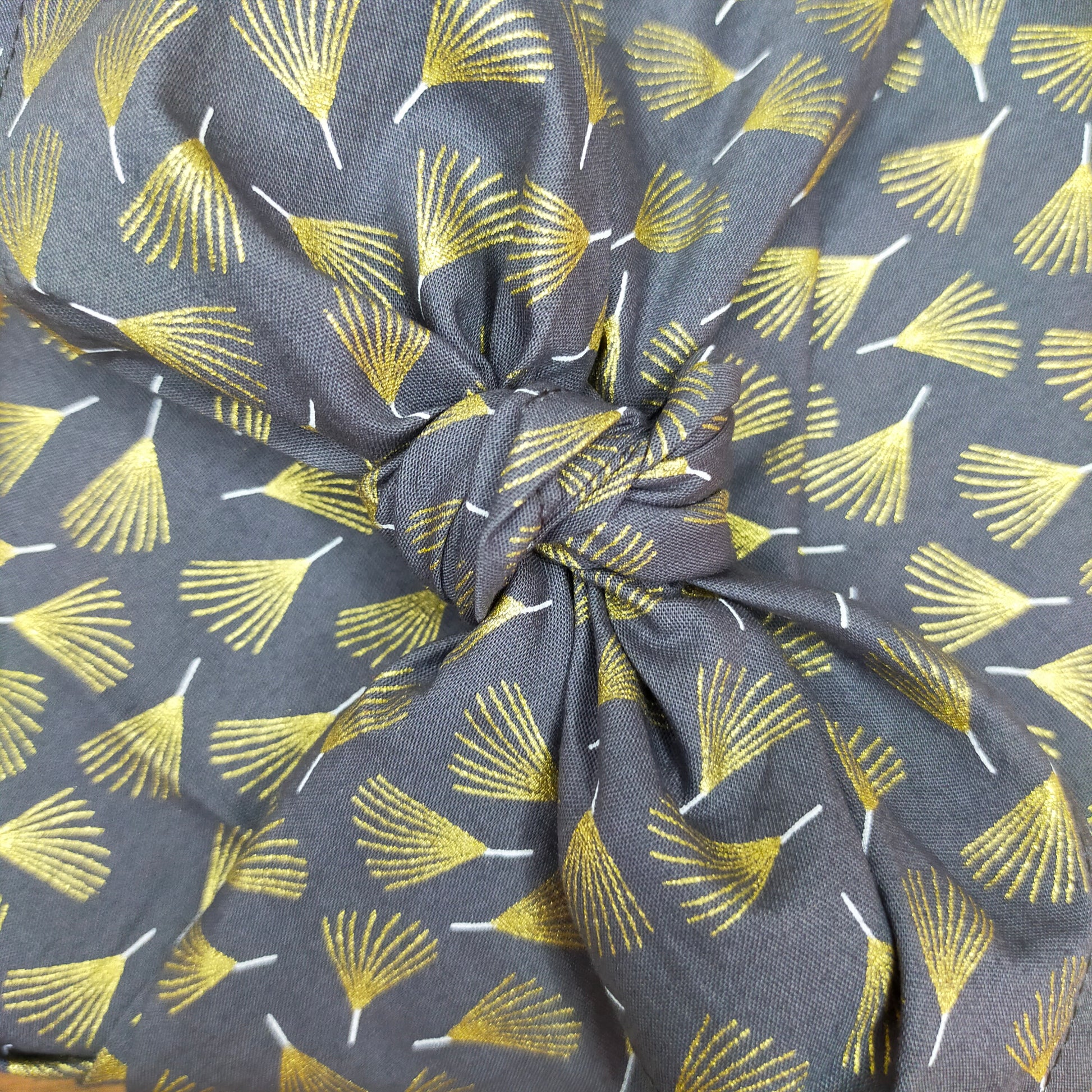 zoom sur le noeud du furoshiki avec le tissu gris aux motifs de feuilles dorées. emballage cadeau écologique et réutilisable