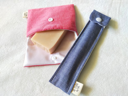 vue de dessus d'une pochette à savon  rose unie ouverte avec un savon à l'intérieur et d'un étui brosse à dent assorti de couleur blue jean.