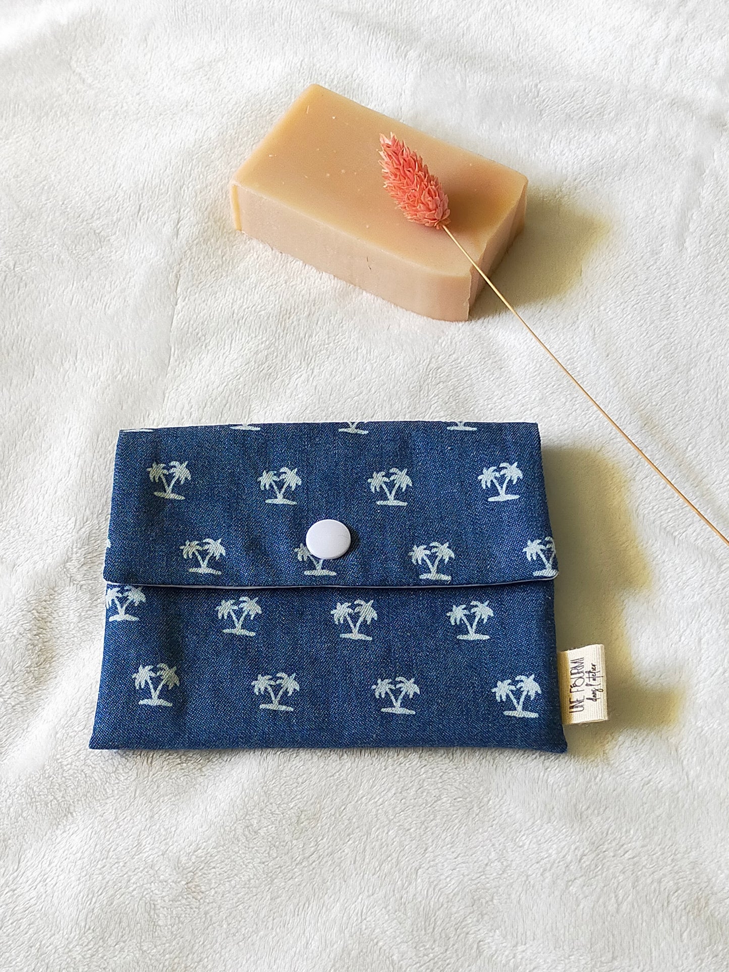 Vue de dessus de la pochette à savon couleur blue jean avec les motifs de palmiers. Fermeture avec une pression blanche.