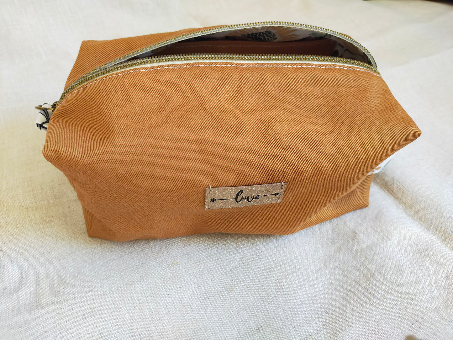 Trousse de toilette en gabardine de coton de couleur jaune moutarde. Fermeture éclaire bronze et patch en cuir recyclé cousu sur l'avant.