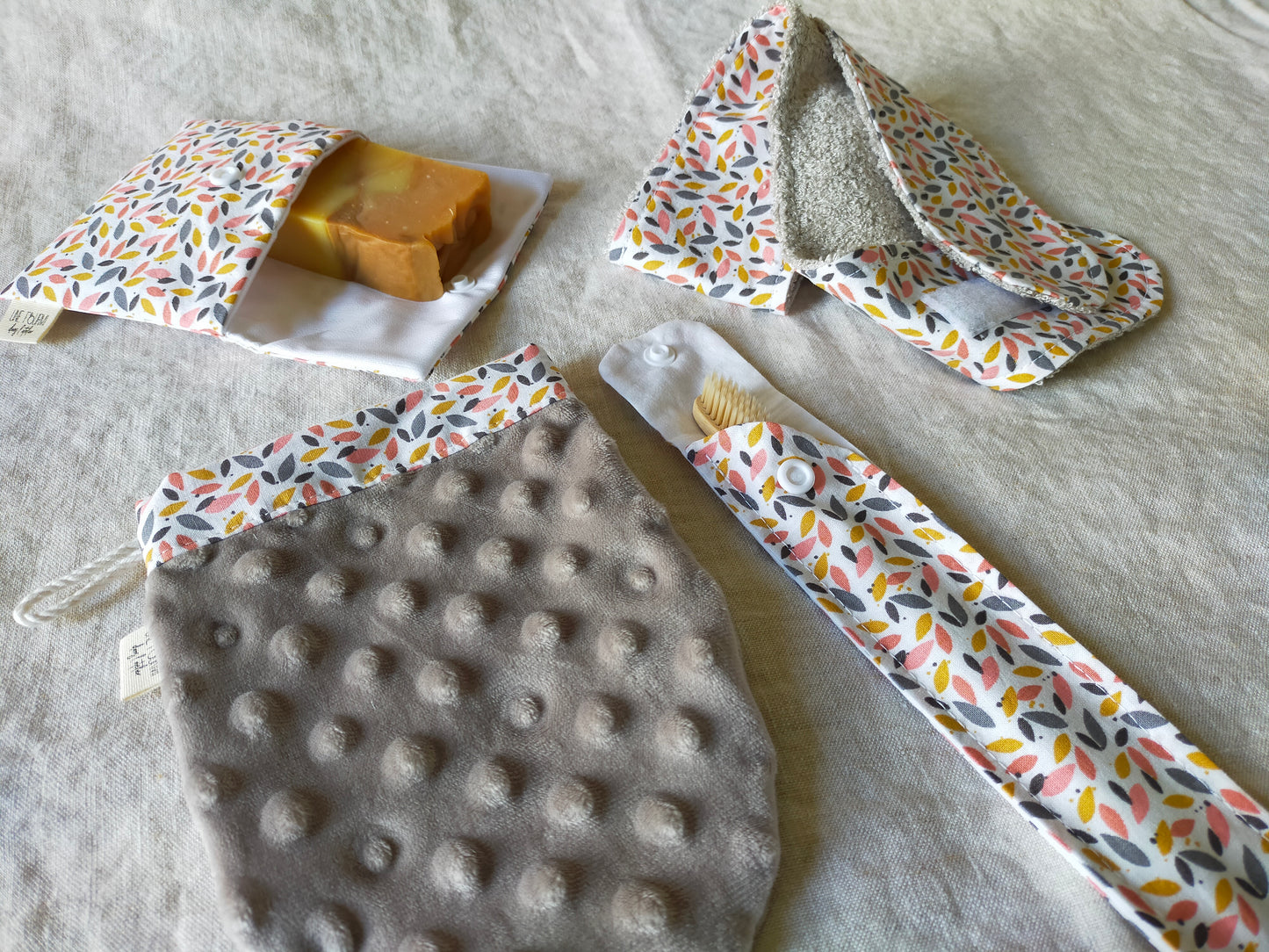 set de toilette de 4 accessoires, pochette à savon, bandeau de soin, étui brosse à dent et gant démaquillant en microfibres. Tons rose et gris avec un motif de feuillage.