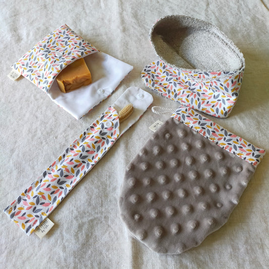 set de toilette de 4 accessoires, pochette à savon, bandeau de soin, étui brosse à dent et gant démaquillant en microfibres. Tons rose et gris avec un motif de feuillage.