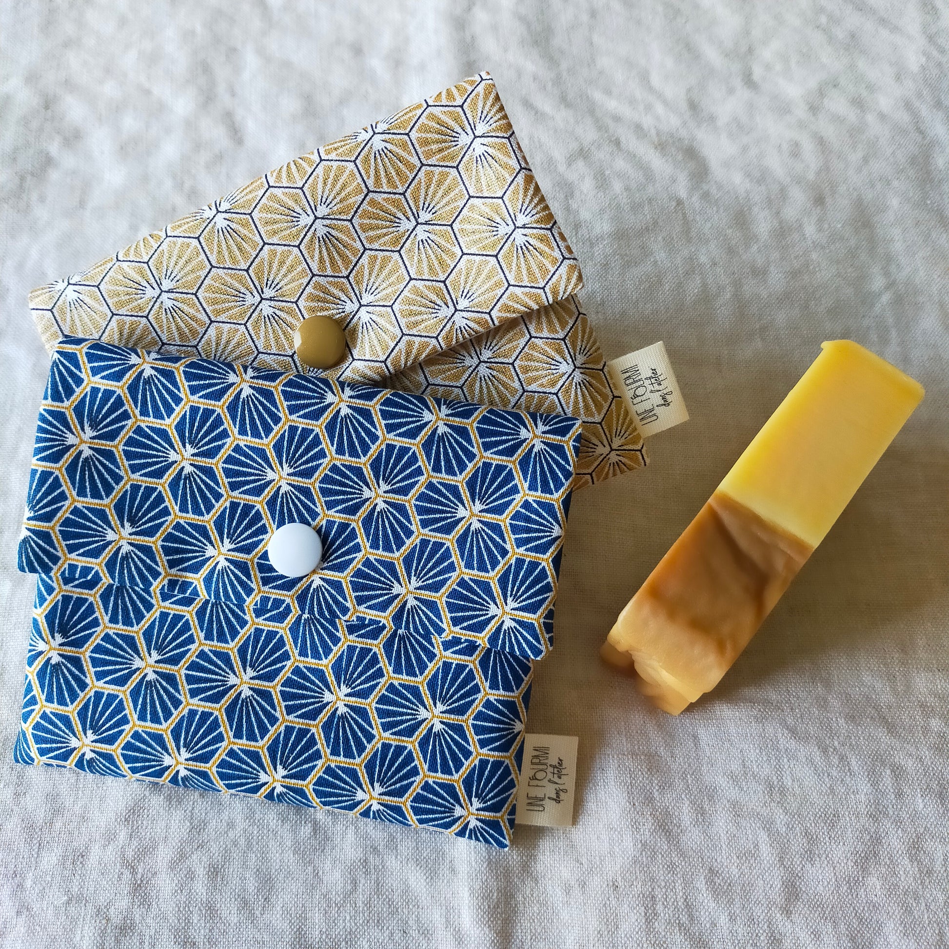 2 pochettes à savon  imperméables. l'une de couleur bleu l'autre de couleur doré et aux motifs géométriques fermeture par pression. accessoire de voyage utile et pratique. consommation responsable et zéro déchet