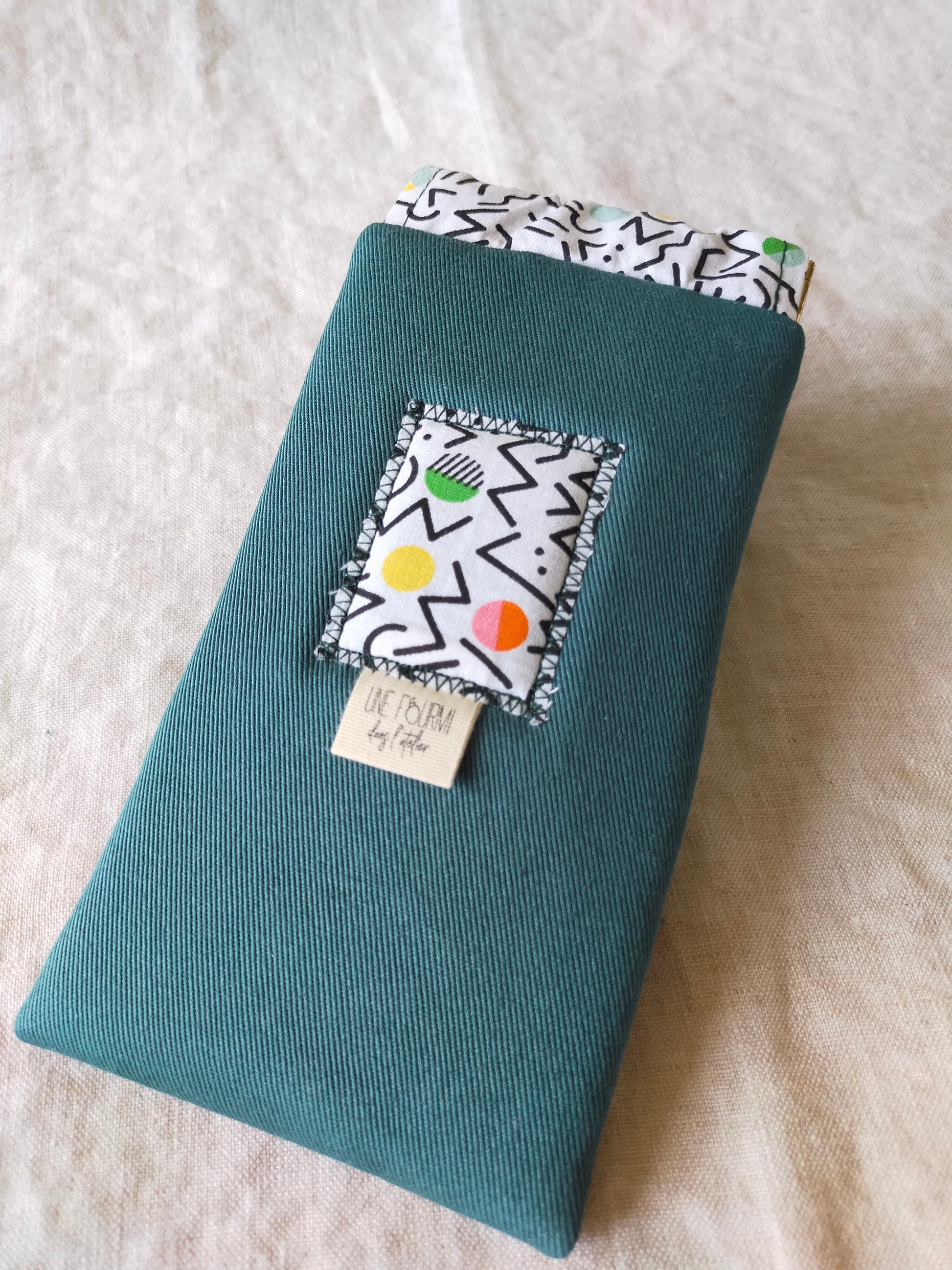 Etui à lunette en coton couleur bleu canard. patch sur l'avant qui rappel les motifs de la doublure très graphiques et coloré. Etiquette de la marque Une fourmi dans l'atelier