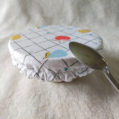 mini charlotte couvre bol pour ramequin et petit récipient de cuisine. accessoire zéro déchet pratique et utile. tissu fond blanc à carreaux avec des dessins de fruits