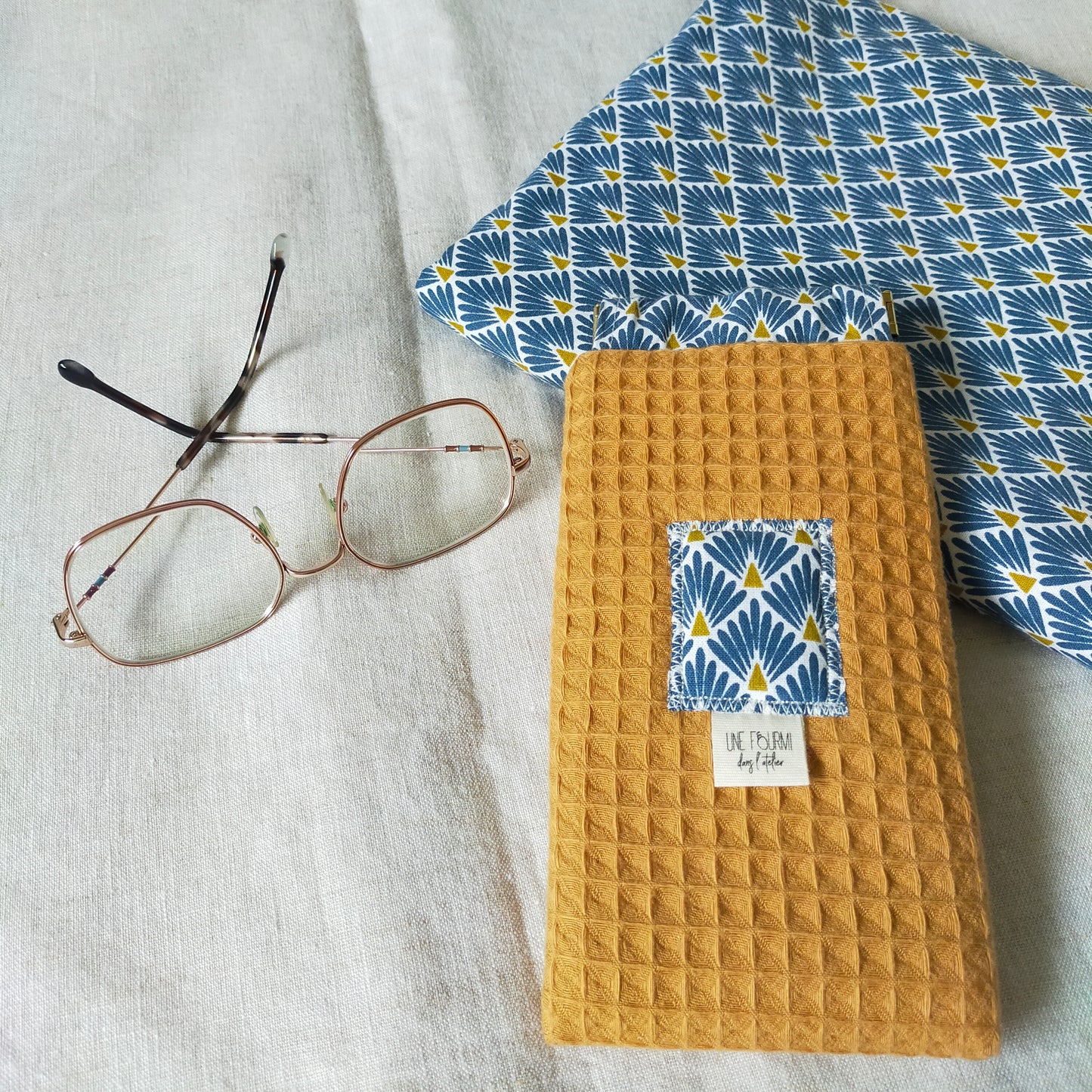 étui à lunettes rembourré, fait en nid d'abeille de couleur jaune moutarde. la doublure est un coton avec motifs géométriques bleus.