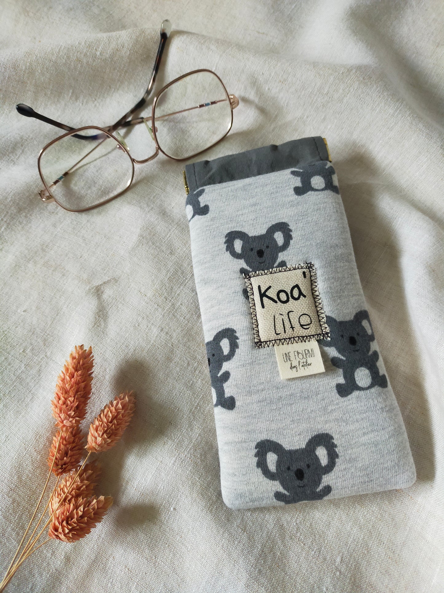 vue dessus, étui à lunette rembourré avec les motifs de Koala et la doublure grise. Patch sur l'avant avec inscription Koa'Life